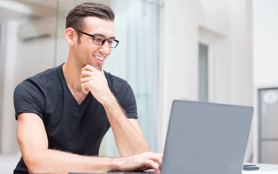 A young male developer smiles as he works on his laptop