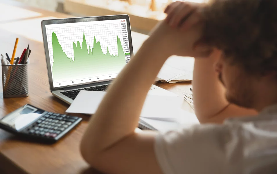 The man stares intently, holding his head as he looks at the graph on his laptop